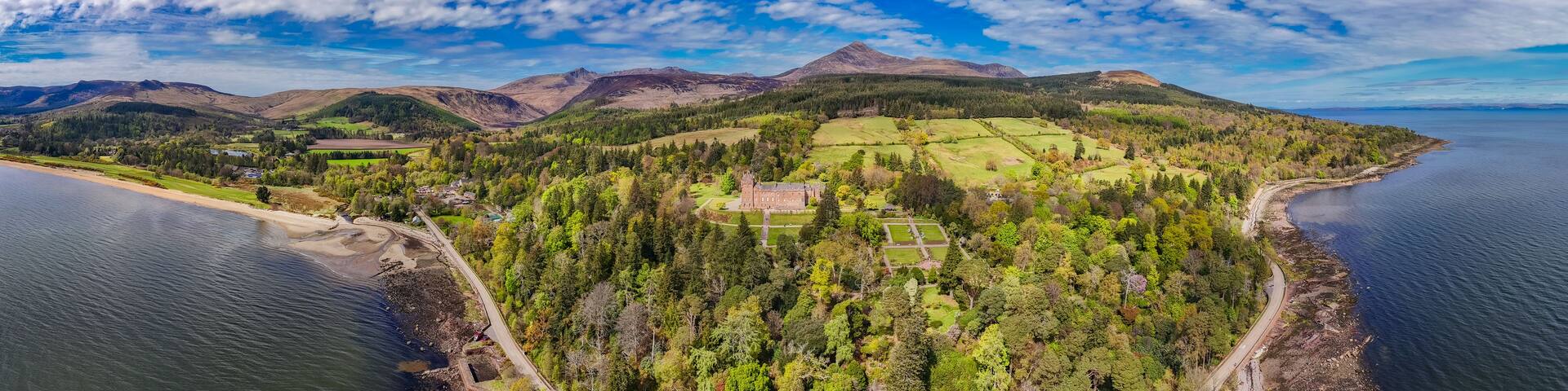 Un paysage côtier avec un château, des collines ondoyantes et une étendue d’eau.