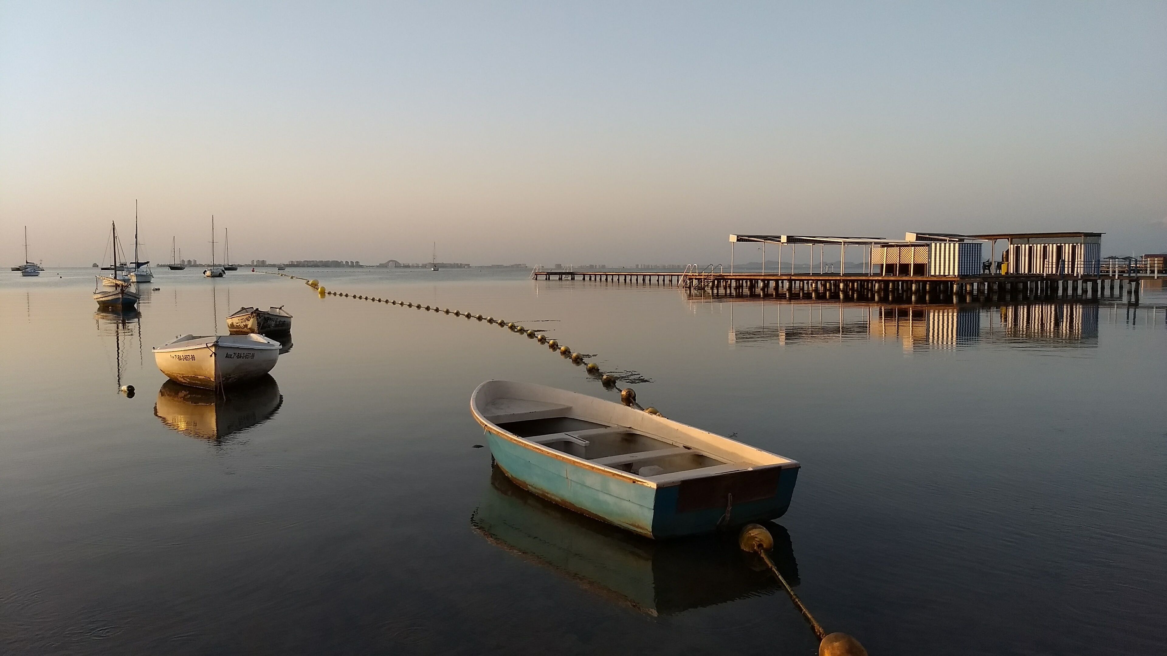 A calm harbor with boats anchored near a wooden pier.