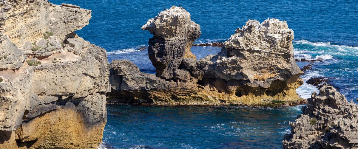 A rugged coastline with prominent rock formations and a clear blue sea.