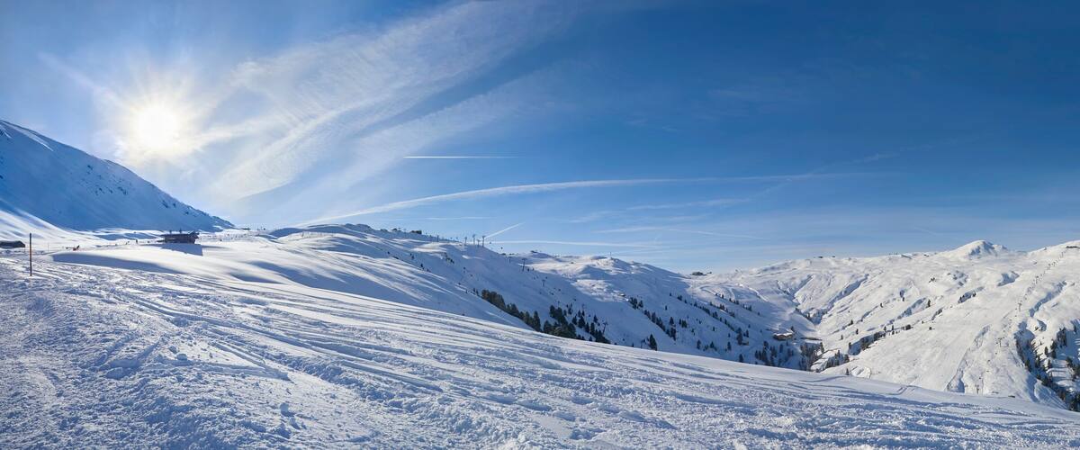 A snow-covered mountain landscape with ski slopes, ski lifts, and a clear blue sky.