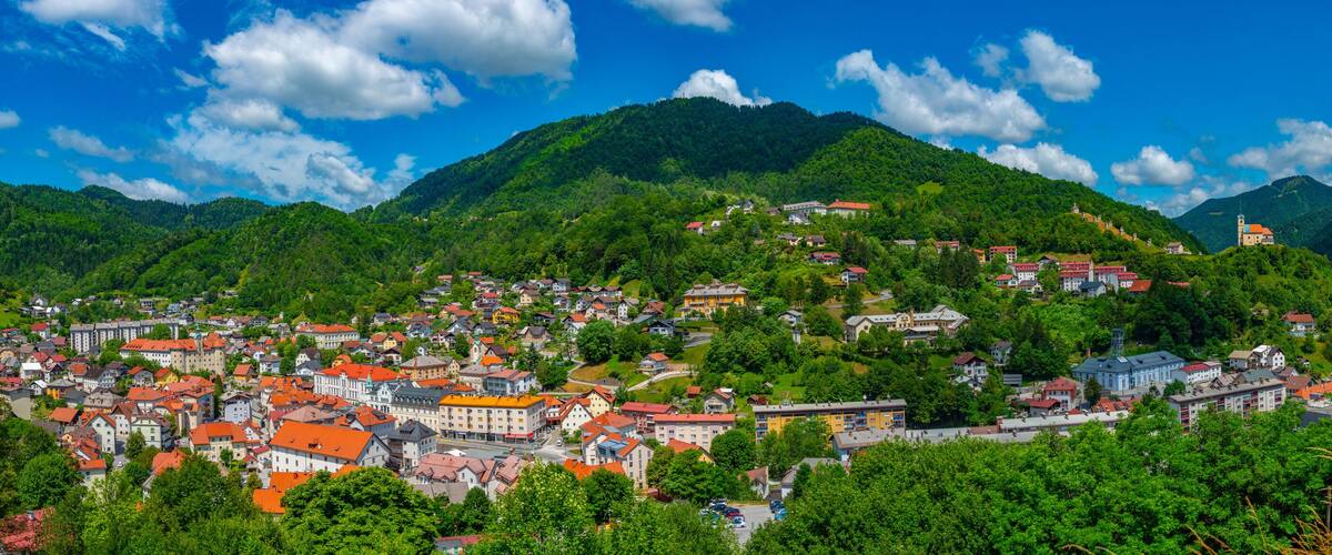 A town nestled in a valley with red-roofed buildings, surrounded by lush green hills and mountains.