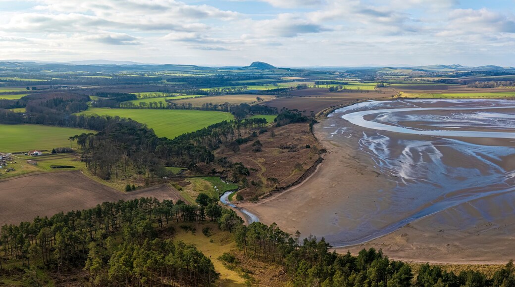Aerial view of a scenic meandering river surrounded by beautiful fields, forests, and hills under a clear sky with clouds, John Muir Country Park, East Lothian, Scotland, United Kingdom.