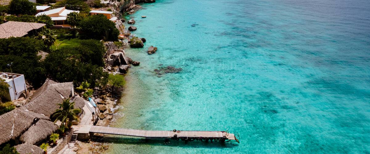 A coastal town with turquoise waters, a wooden pier, and houses with red roofs.