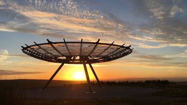 A large circular structure with a metal frame, set against a sunset sky with scattered clouds.
