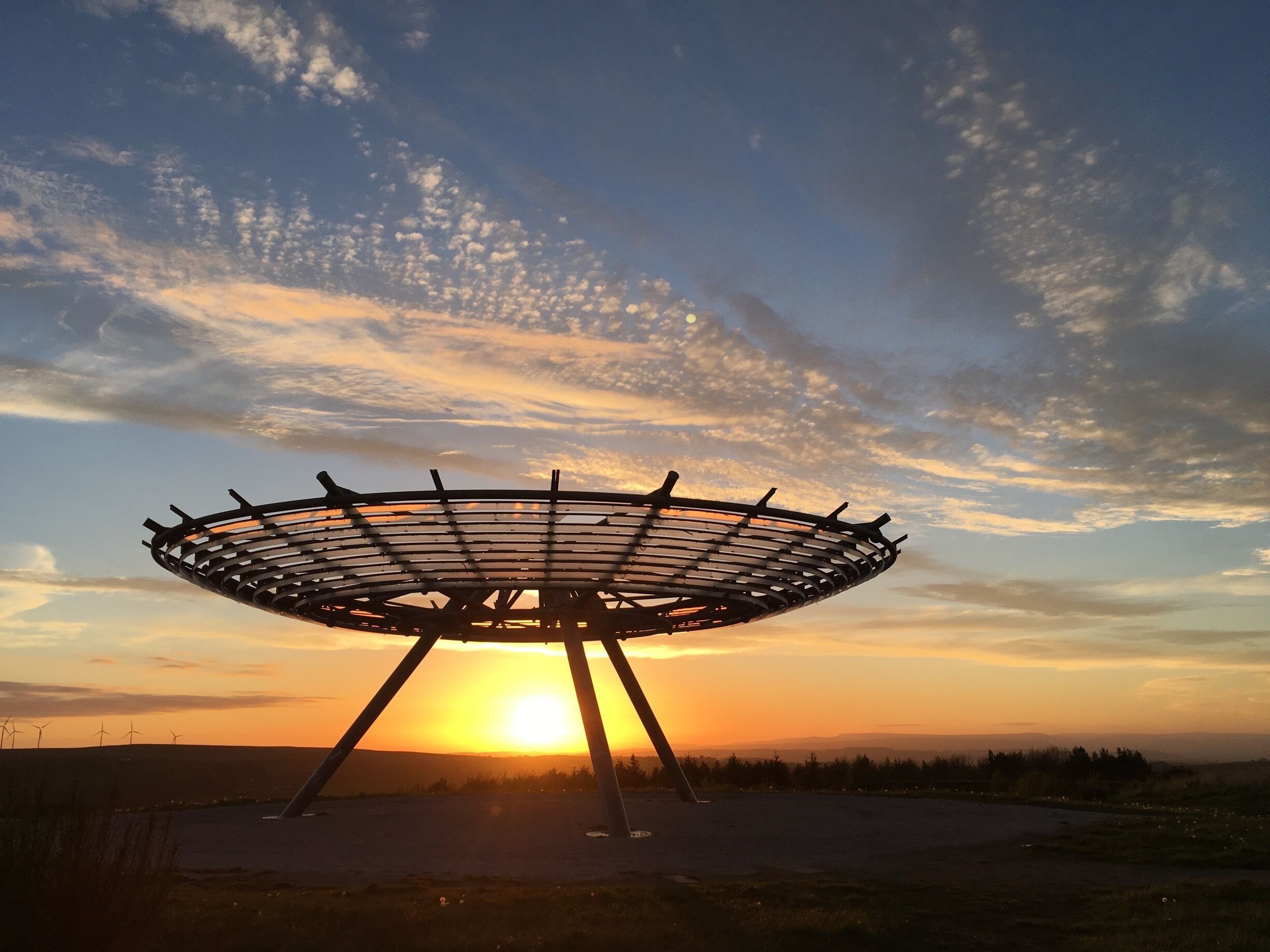 A large circular structure with a metal frame, set against a sunset sky with scattered clouds.