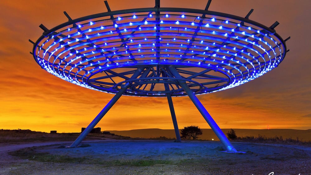 A large, illuminated structure with a circular design, set against a sunset sky.
