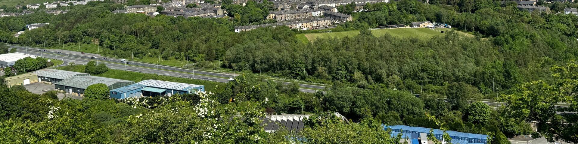 A town with a mix of residential and industrial buildings, surrounded by green hills and a clear blue sky.