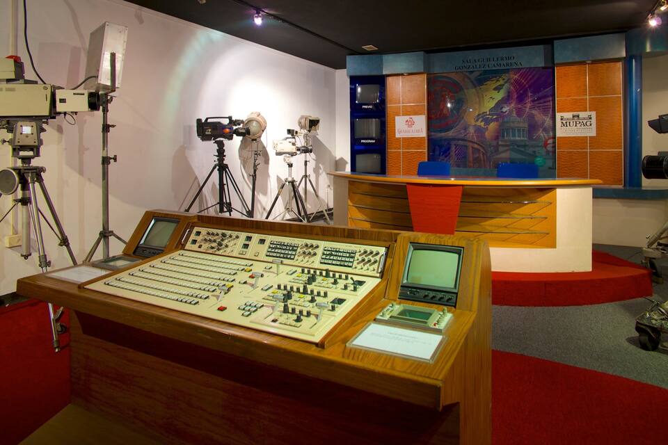 A control room with various technical equipment, including a large control panel, multiple screens, and communication devices.