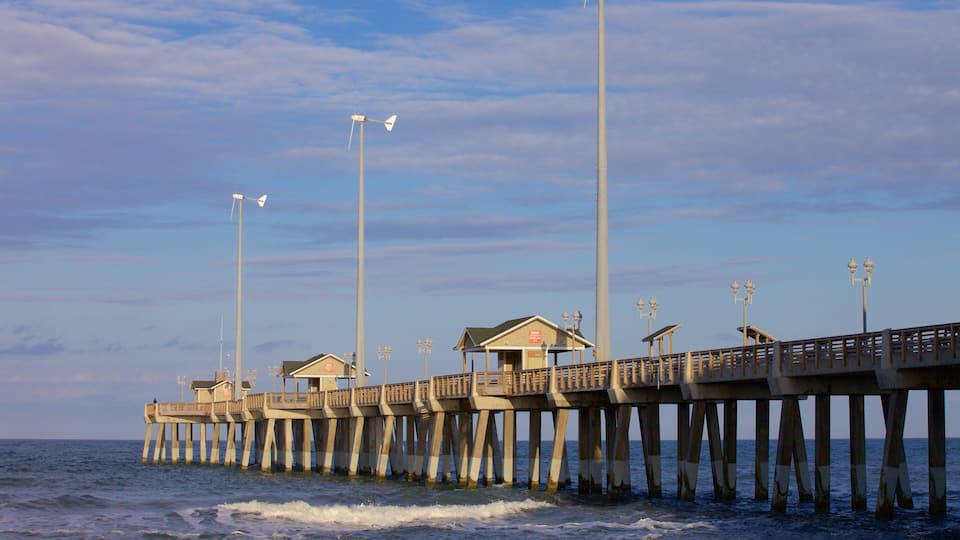 A pier extending into the ocean with a small building and street lamps.