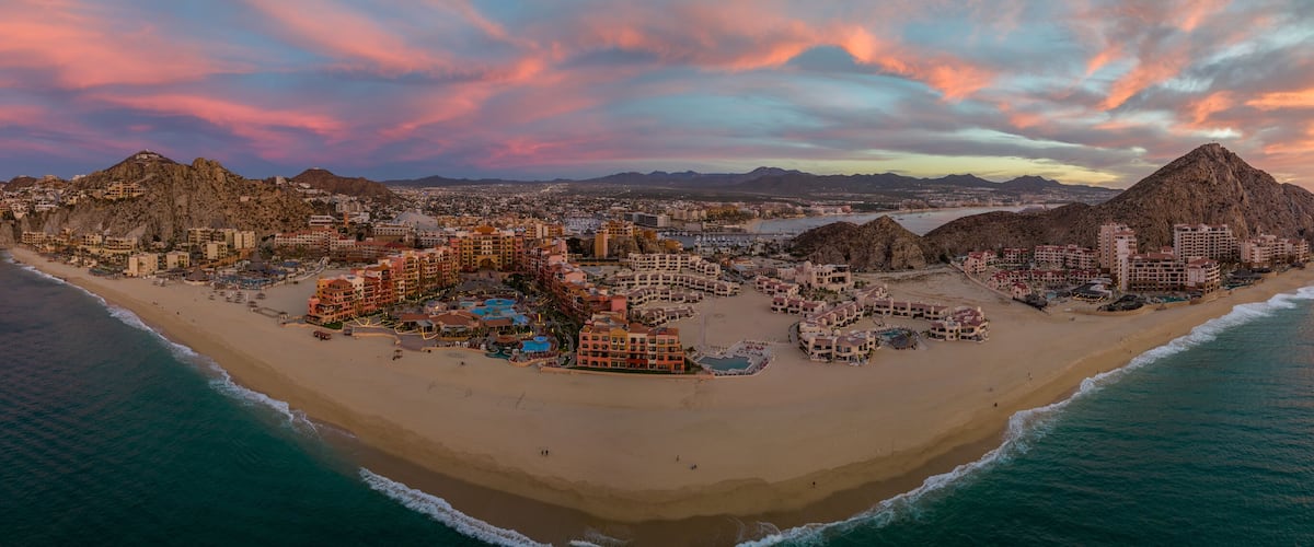 A coastal cityscape with a beach, hotels, and mountains.