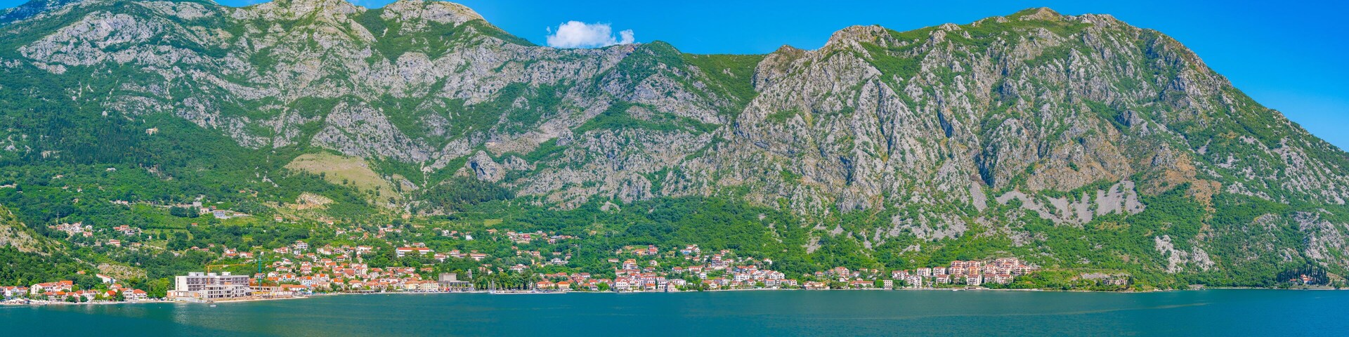 Uma vila costeira com edifícios ao longo da orla, rodeada por colinas e montanhas verdes.