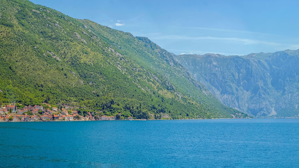 A coastal town with red-roofed buildings, a large body of water, and a mountain range in the background.