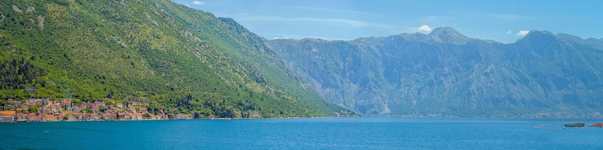 A coastal town with red-roofed buildings, a large body of water, and a mountain range in the background.