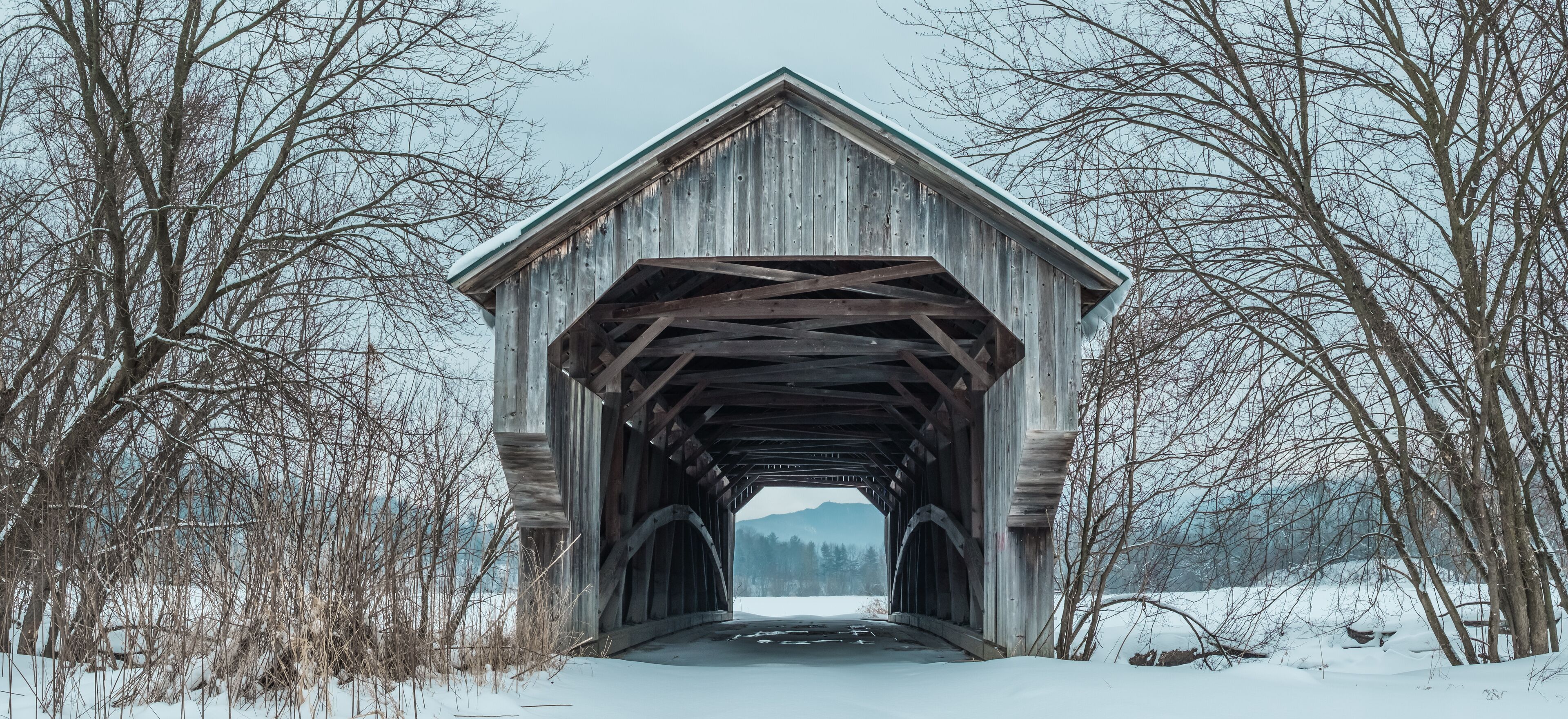 A wooden covered bridge in a snowy landscape with bare trees.