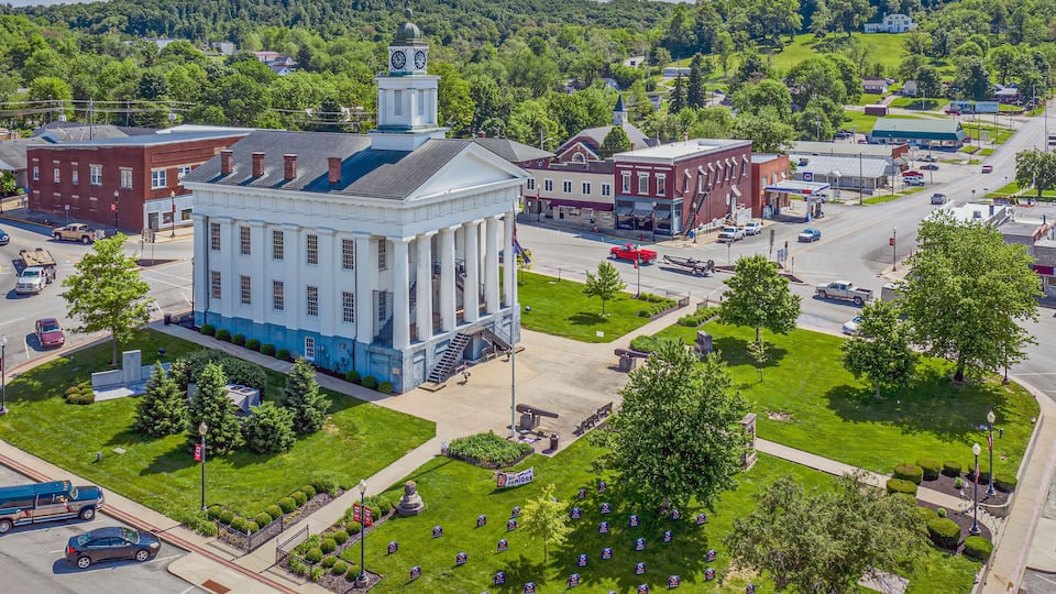 A courthouse surrounded by green lawns and trees, with a clock tower and a statue in front.