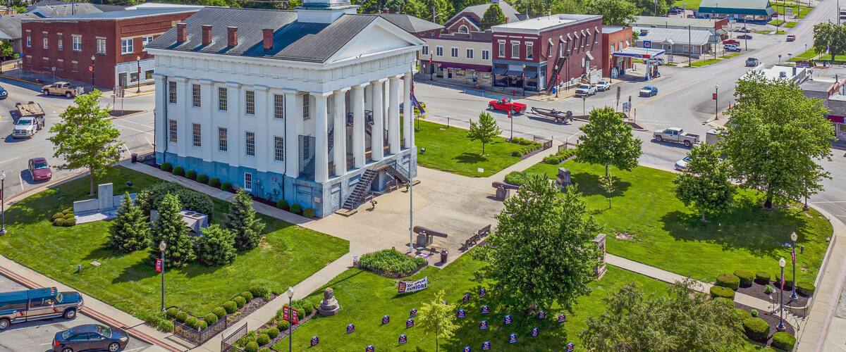 A courthouse surrounded by green lawns and trees, with a clock tower and a statue in front.