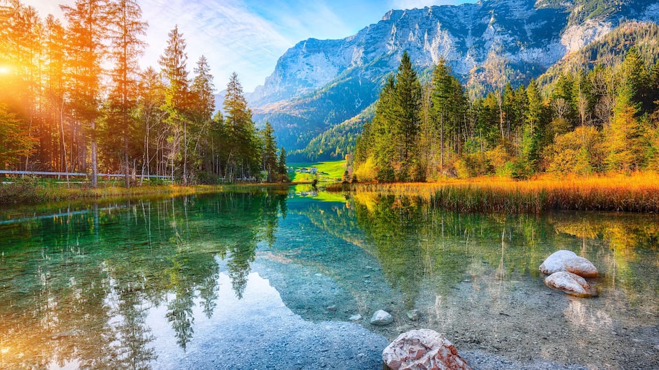A clear mountain lake surrounded by evergreen trees and a rugged mountain backdrop.