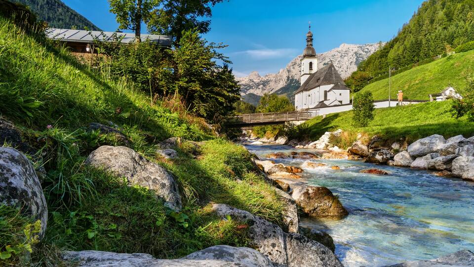 A river flowing through a valley with a church and a bridge.