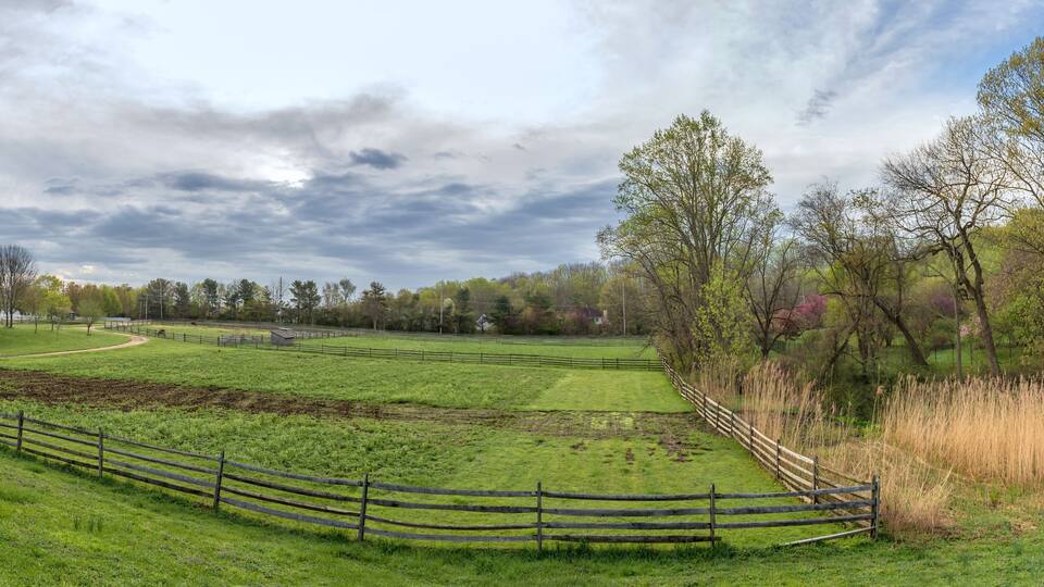 A rural landscape with a barn, fenced fields, and a winding path.