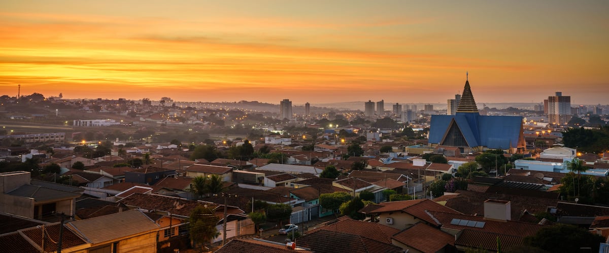 A cityscape at sunset with a prominent church spire and a modern building with a blue roof.