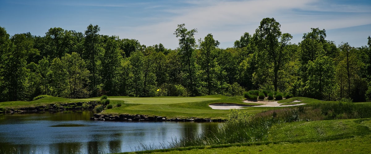 A golf course with a pond, sand bunkers, and a forested background.