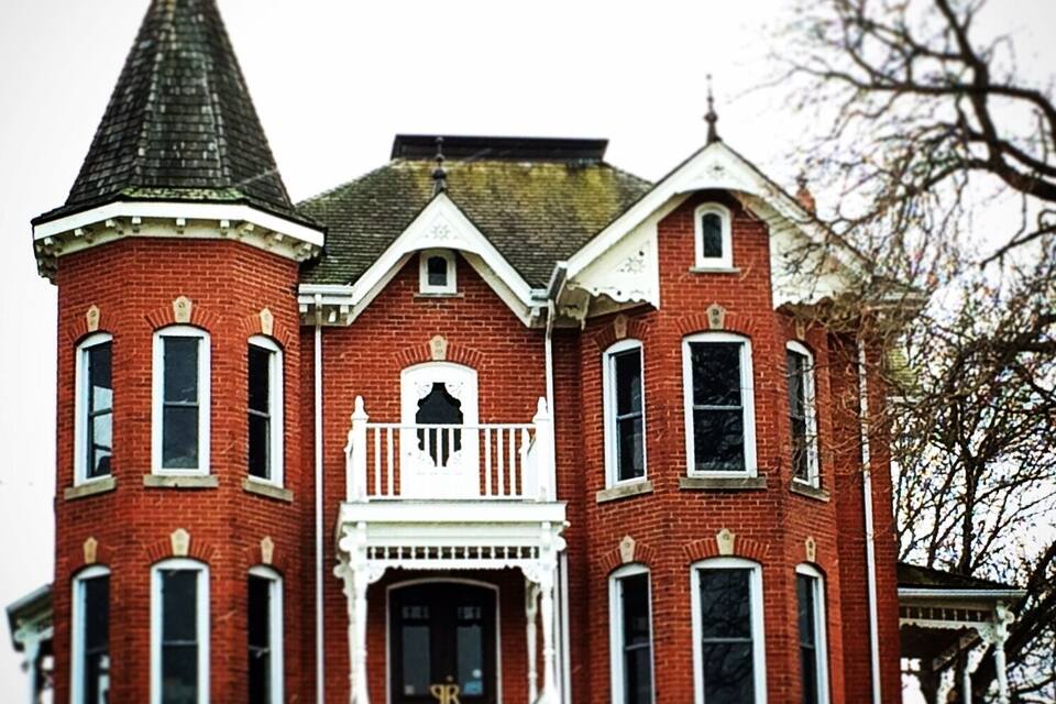 A large red brick building with a tower, a central entrance with a white porch, and a small balcony.