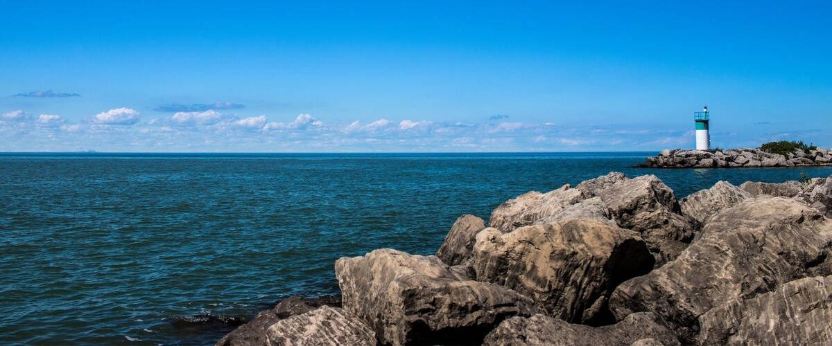 A rocky shoreline with a lighthouse on a small island in the distance.