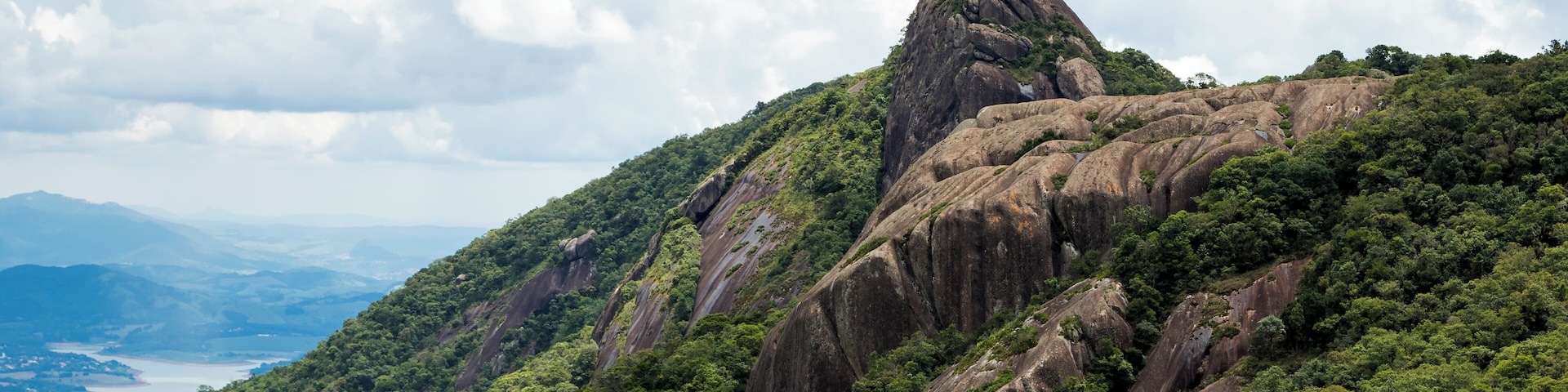 horizontal view of a mountain rock face with some trees under a blue sky with white clouds - pico e serra do lopo