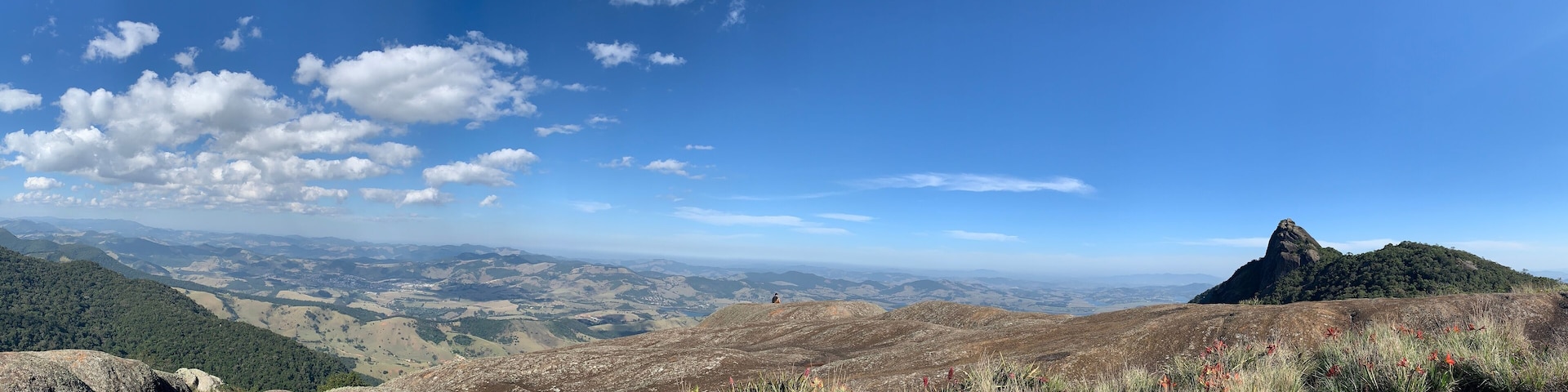 Un paisaje montañoso con un pico destacado, colinas ondulantes y un cielo azul despejado.