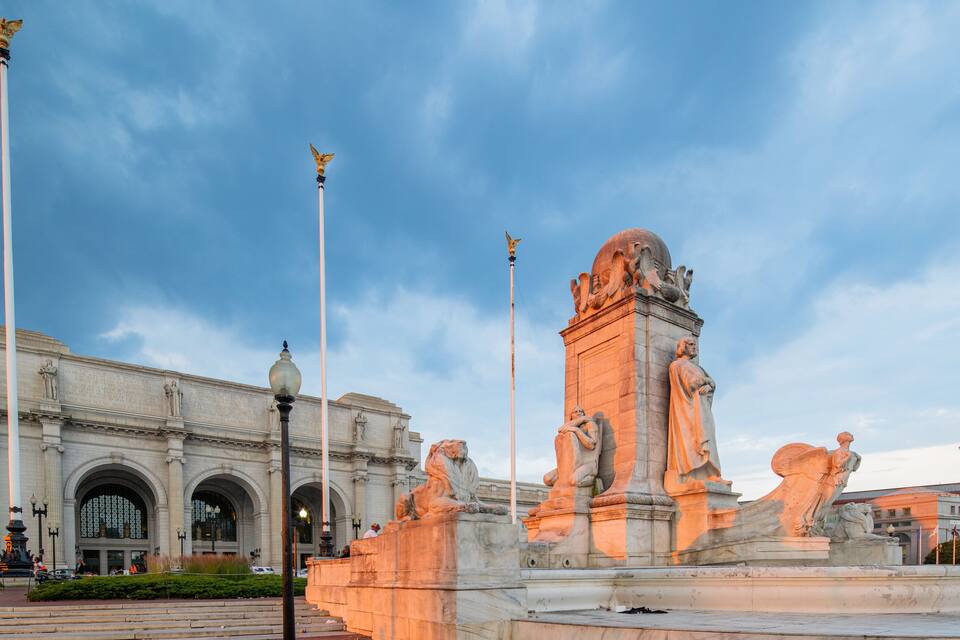 Um edifício imponente com janelas em arco e uma grande estátua em primeiro plano.