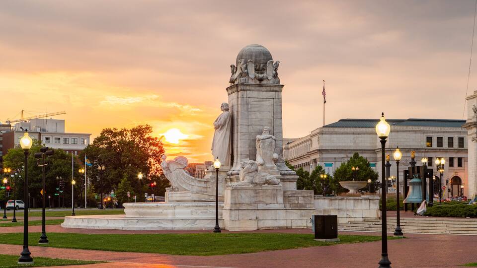 A statue of a man with a globe at the top, surrounded by lions, with a sunset in the background.