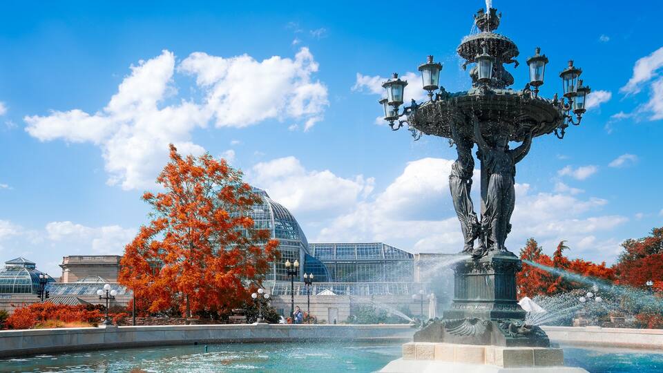 Eine Fontäne mit Wasserstrahlen, eine Statue und ein Glasgebäude im Hintergrund.