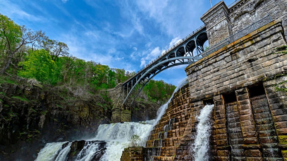 A dam with a bridge, waterfalls, and a forested hillside.