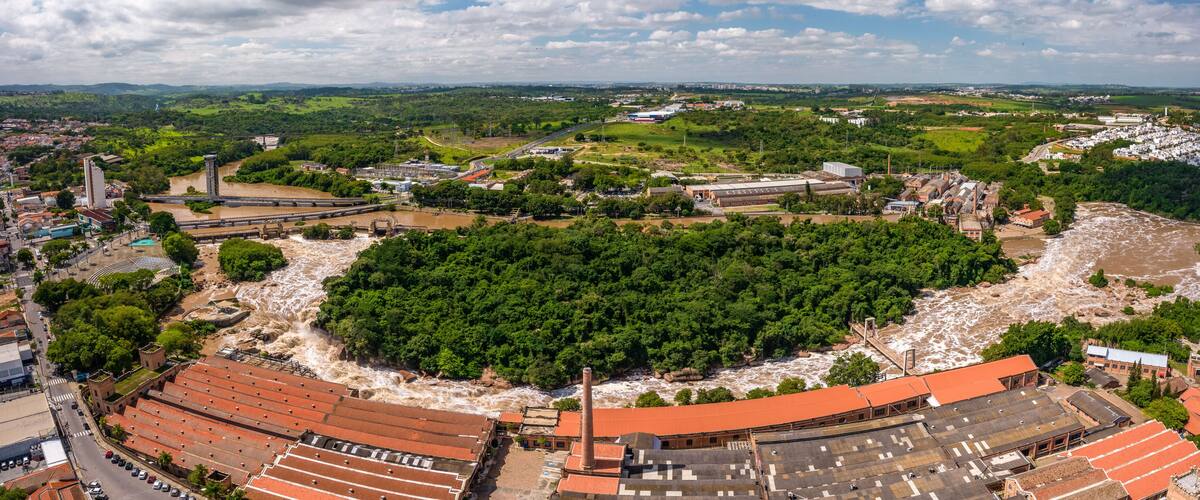 A river flowing through a town with industrial buildings and a large forested area.