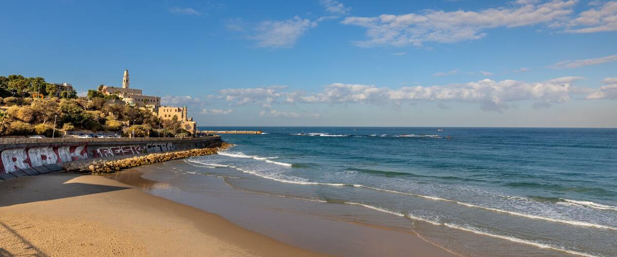 A coastal landscape with a beach, waves, a lighthouse, and a building with graffiti.