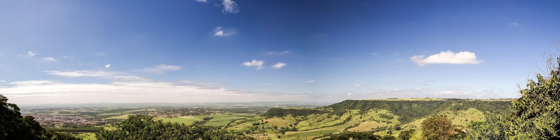 A panoramic view of a lush green valley with rolling hills and a clear blue sky.