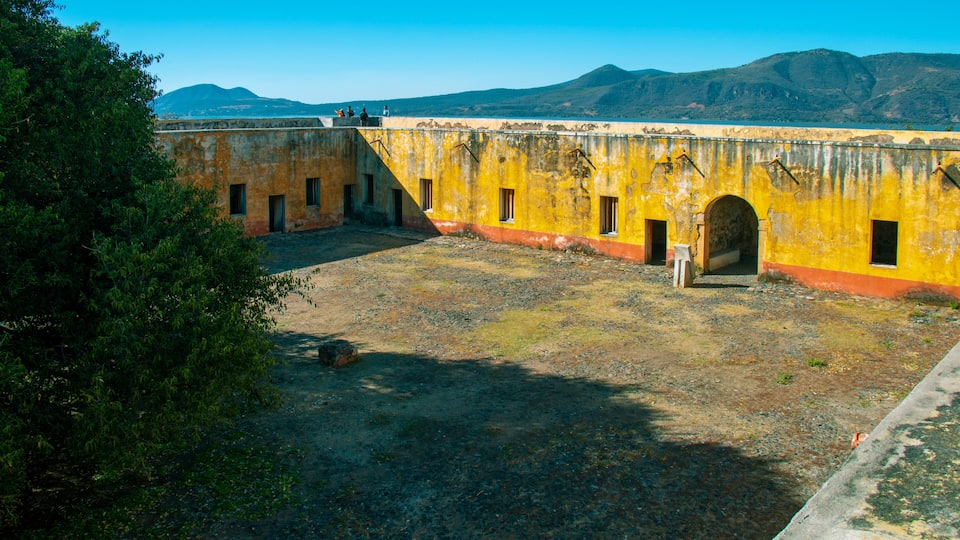 An old yellow building with arched doorways and a clear blue sky in the background.