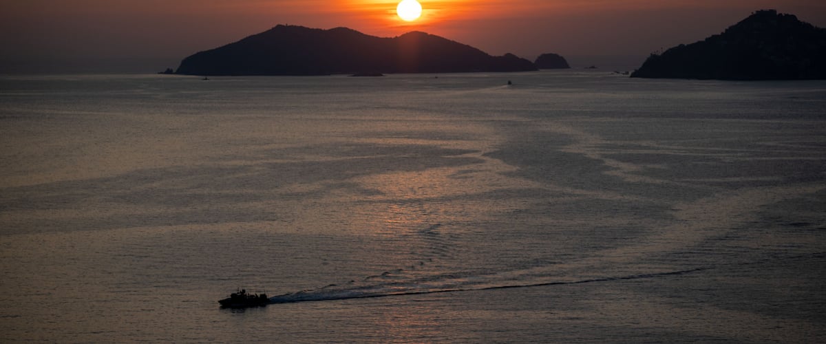 A sunset over a calm sea with distant islands.