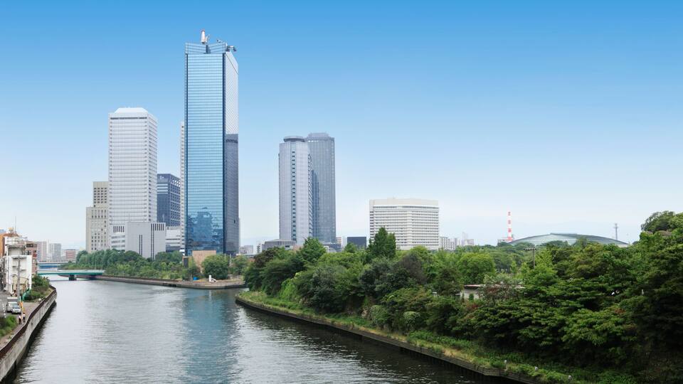 A river with a bridge, surrounded by greenery and tall buildings.