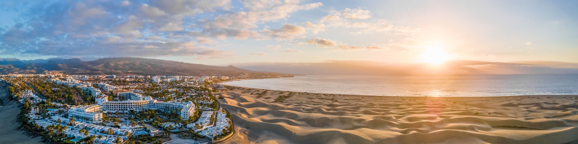 A coastal resort with sand dunes and a sunset over the ocean.