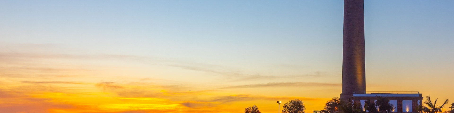 Atardecer costero con un faro y una playa.