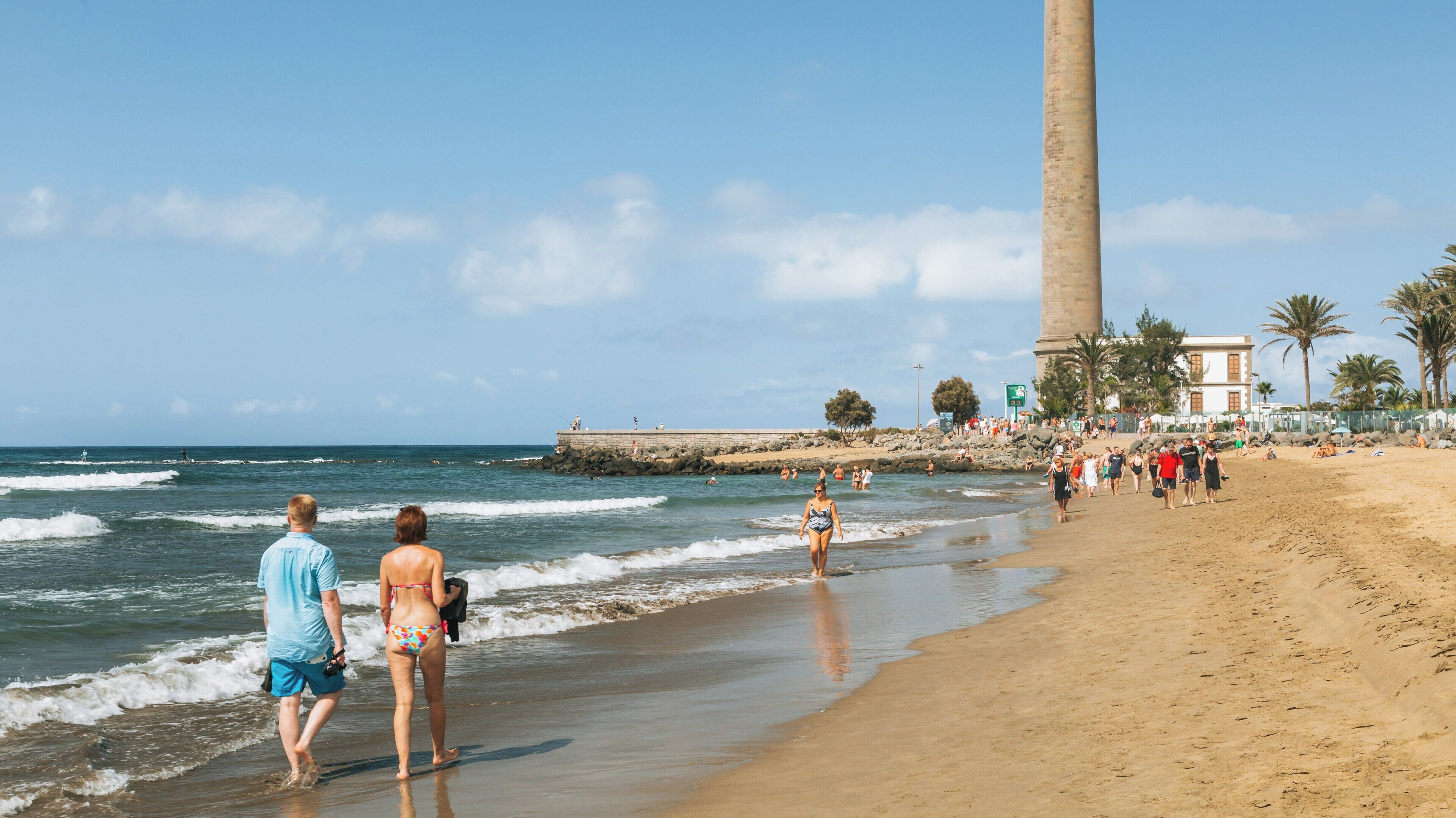 Visitors stroll along the sandy beach near Maspalomas Lighthouse in San Bartolome de Tirajana on a sunny day in the Canary Islands