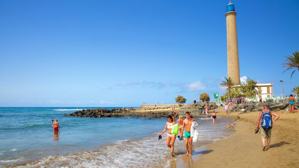 A beach with people walking along the shore, a lighthouse, and rocky outcrops.