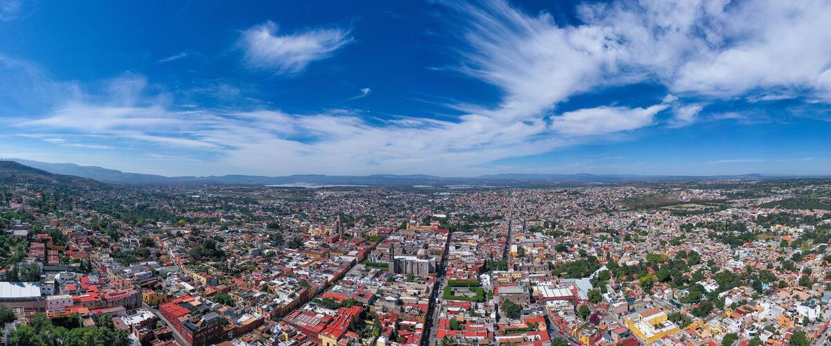 A panoramic view of a city with a dense urban area, green hills in the background, and a clear blue sky.