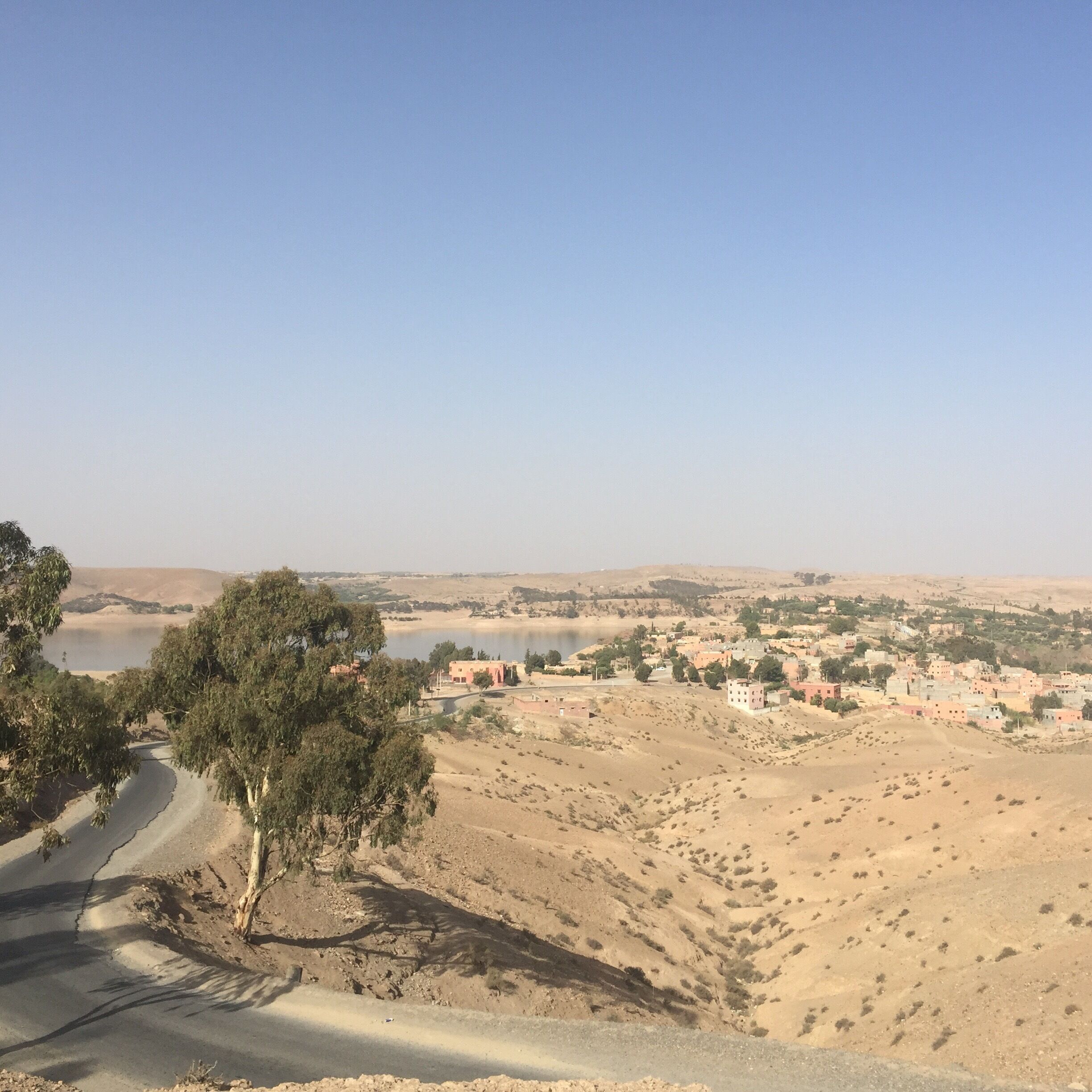 A desert landscape with a road, a body of water, and a town in the distance.