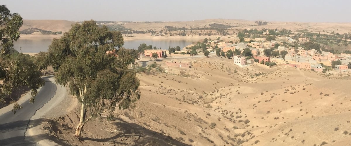 A desert landscape with a road, a body of water, and a town in the distance.