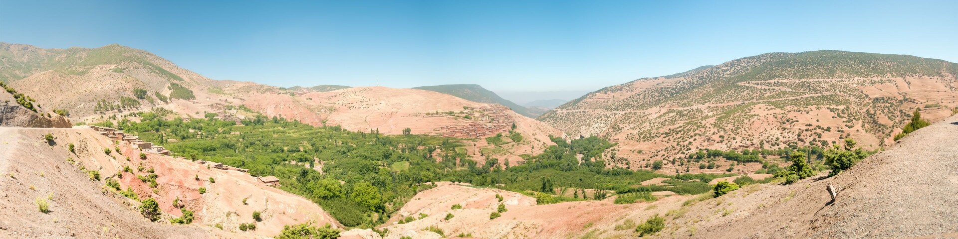 Paisagem montanhosa com um vale, campos em socalcos e árvores dispersas.