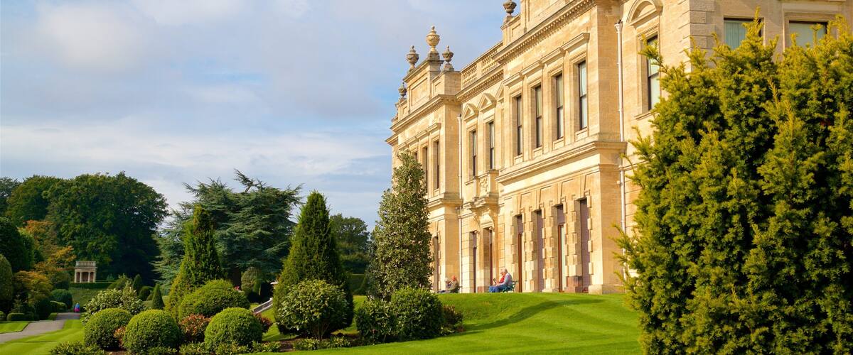A grand historic building with ornate architecture, surrounded by lush greenery and a well-maintained garden.