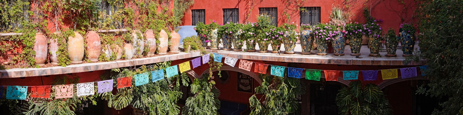 Un patio con paredes rojas, macetas de barro grandes y plantas colgantes.