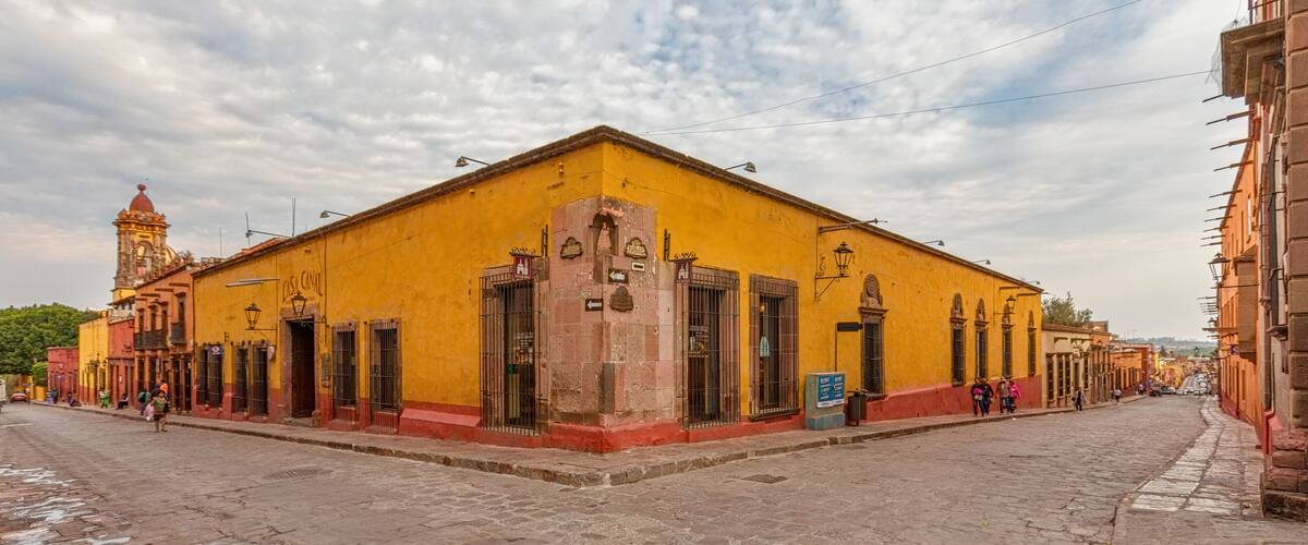 A yellow building with a clock tower, cobblestone street, and pedestrians.